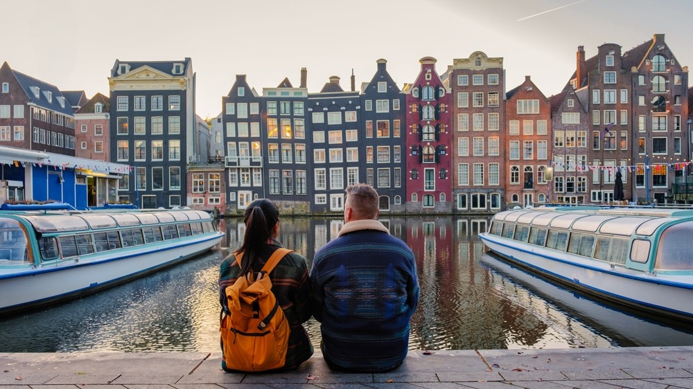 What expat couples in The Netherlands only often discover too late. Couple sitting next to a canal in Amsterdam, across traditional Dutch houses.